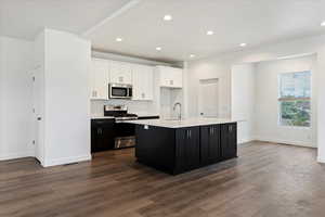 Kitchen featuring hardwood / wood-style floors, a center island with sink, sink, white cabinetry, and appliances with stainless steel finishes