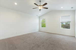 Carpeted empty room with ceiling fan and lofted ceiling