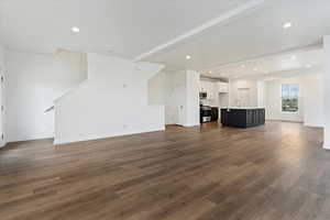 Unfurnished living room featuring beam ceiling, sink, and dark wood-type flooring