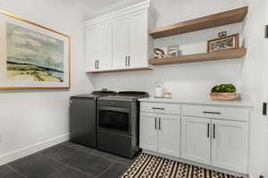 Laundry area with cabinets, dark tile floors, and washing machine and clothes dryer