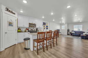 Kitchen featuring light stone countertops, light wood-type flooring, a center island with sink, appliances with stainless steel finishes, and white cabinets