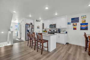 Kitchen featuring light stone counters, a kitchen island, stainless steel appliances, white cabinetry, and light wood-type flooring