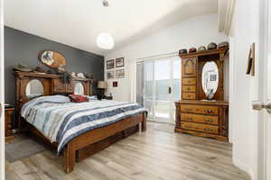 Bedroom with vaulted ceiling, light wood-type flooring, and access to outside