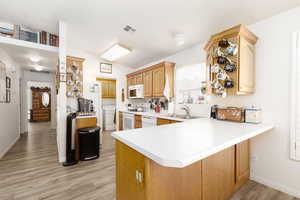 Kitchen with light hardwood / wood-style floors, white appliances, kitchen peninsula, sink, and vaulted ceiling