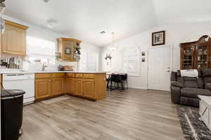 Kitchen featuring vaulted ceiling, kitchen peninsula, white dishwasher, light wood-type flooring, and pendant lighting