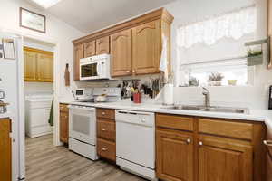 Kitchen featuring sink, white appliances, light wood-type flooring, and washer / clothes dryer