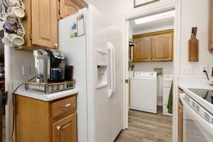 Kitchen featuring washing machine and clothes dryer, light hardwood / wood-style flooring, and white refrigerator with ice dispenser