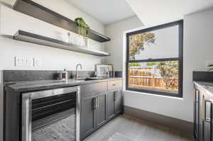 Kitchen with beverage cooler, sink, dark stone counters, and wood-type flooring