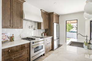 Kitchen with premium appliances, light wood-type flooring, backsplash, sink, and custom exhaust hood