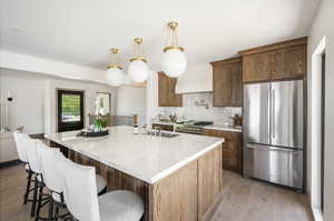 Kitchen featuring stainless steel appliances, hanging light fixtures, a center island with sink, tasteful backsplash, and wood-type flooring