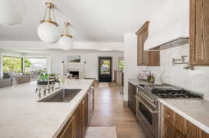 Kitchen with light hardwood / wood-style floors, tasteful backsplash, pendant lighting, custom range hood, and appliances with stainless steel finishes