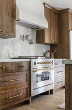 Kitchen with stainless steel appliances, custom range hood, light hardwood / wood-style flooring, and tasteful backsplash