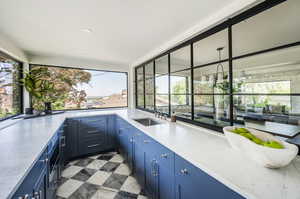 Kitchen with blue cabinets, light stone countertops, sink, and light tile floors