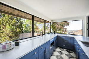 Kitchen with stainless steel microwave, blue cabinetry, light stone counters, oven, and light tile flooring