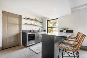 Kitchen featuring light hardwood / wood-style floors, beverage cooler, kitchen peninsula, a kitchen bar, and sink