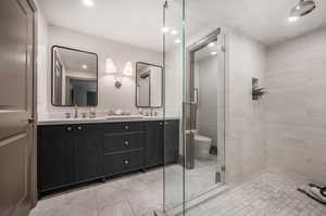 Bathroom featuring walk in shower, tile floors, oversized vanity, toilet, and dual sinks