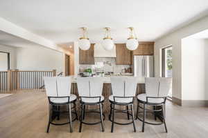 Kitchen with a kitchen breakfast bar, light wood-type flooring, high end refrigerator, decorative light fixtures, and tasteful backsplash