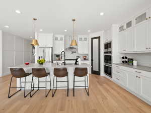 Kitchen with light hardwood / wood-style floors, appliances with stainless steel finishes, tasteful backsplash, and a kitchen island with sink