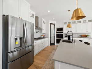 Kitchen with backsplash, stainless steel appliances, light hardwood / wood-style floors, sink, and wall chimney range hood