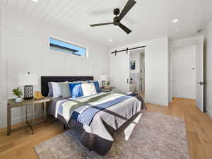 Bedroom featuring ceiling fan, light wood-type flooring, and a barn door