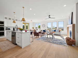 Kitchen featuring light hardwood / wood-style flooring, white cabinets, appliances with stainless steel finishes, sink, and a center island with sink