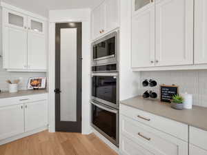 Kitchen featuring backsplash, appliances with stainless steel finishes, white cabinets, and light hardwood / wood-style flooring