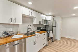 Kitchen with stainless steel appliances, white cabinets, backsplash, and light wood-type flooring