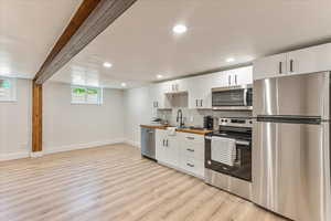 Kitchen with white cabinetry, light hardwood / wood-style flooring, appliances with stainless steel finishes, backsplash, and sink