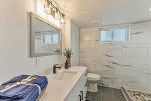 Bathroom featuring tile walls, toilet, a tile shower, tile flooring, and vanity