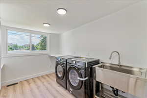 Clothes washing area featuring sink, washing machine and dryer, and light wood-type flooring