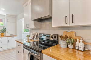 Kitchen featuring white cabinets, stainless steel range with electric cooktop, and custom exhaust hood