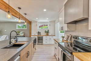 Kitchen with white cabinetry, light wood-type flooring, stainless steel appliances, wine cooler, and sink