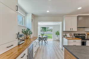 Kitchen with stainless steel range with electric stovetop, tasteful backsplash, wine cooler, white cabinetry, and light wood-type flooring