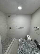 Bathroom with tile floors, tiled shower, a textured ceiling, and toilet