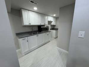 Kitchen featuring sink, white cabinets, dark stone countertops, and light tile floors