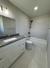 Full bathroom featuring oversized vanity, toilet, tile floors, tiled shower / bath combo, and a textured ceiling