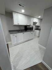 Kitchen featuring white cabinets, sink, light hardwood / wood-style flooring, and dark stone counters