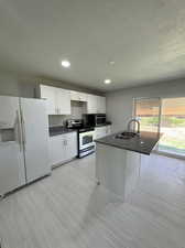 Kitchen featuring appliances with stainless steel finishes, white cabinets, a kitchen island with sink, sink, and light tile floors