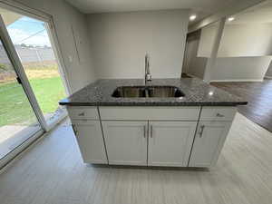 Kitchen featuring sink, white cabinetry, light hardwood / wood-style floors, and dark stone counters