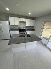 Kitchen featuring sink, white cabinetry, white fridge, and stainless steel range with electric cooktop