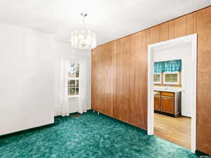 Spare room featuring a notable chandelier, carpet, and wooden walls