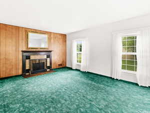 Unfurnished living room featuring wood walls and dark carpet