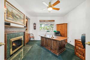 Carpeted office with a fireplace and ceiling fan