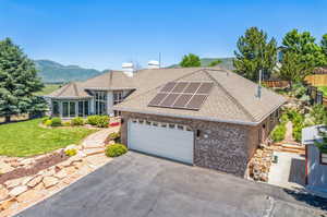 View of front of house with a garage, a mountain view, a front lawn, and solar panels