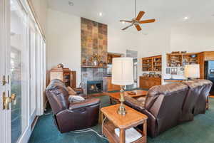 Living room featuring a high ceiling, carpet, ceiling fan, and a fireplace