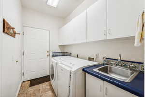 Clothes washing area featuring cabinets, washer hookup, sink, washing machine and dryer, and light tile floors