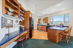 Kitchen featuring kitchen peninsula, black appliances, light colored carpet, sink, and a kitchen bar