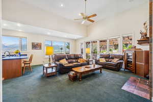 Living room featuring ceiling fan, a towering ceiling, dark colored carpet, and a wealth of natural light