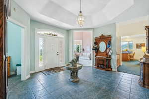 Entrance foyer featuring tile flooring, a tray ceiling, and a chandelier