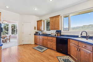 Kitchen with black dishwasher, sink, and light hardwood / wood-style flooring